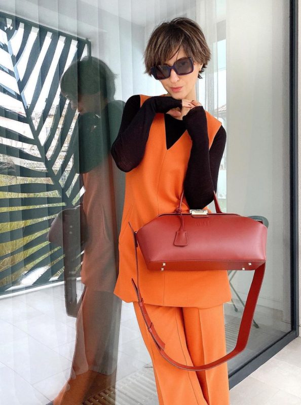 a colorful spring outfit with a black long sleeve top, an orange waistcoat, orange trousers, a red handbag is amazing