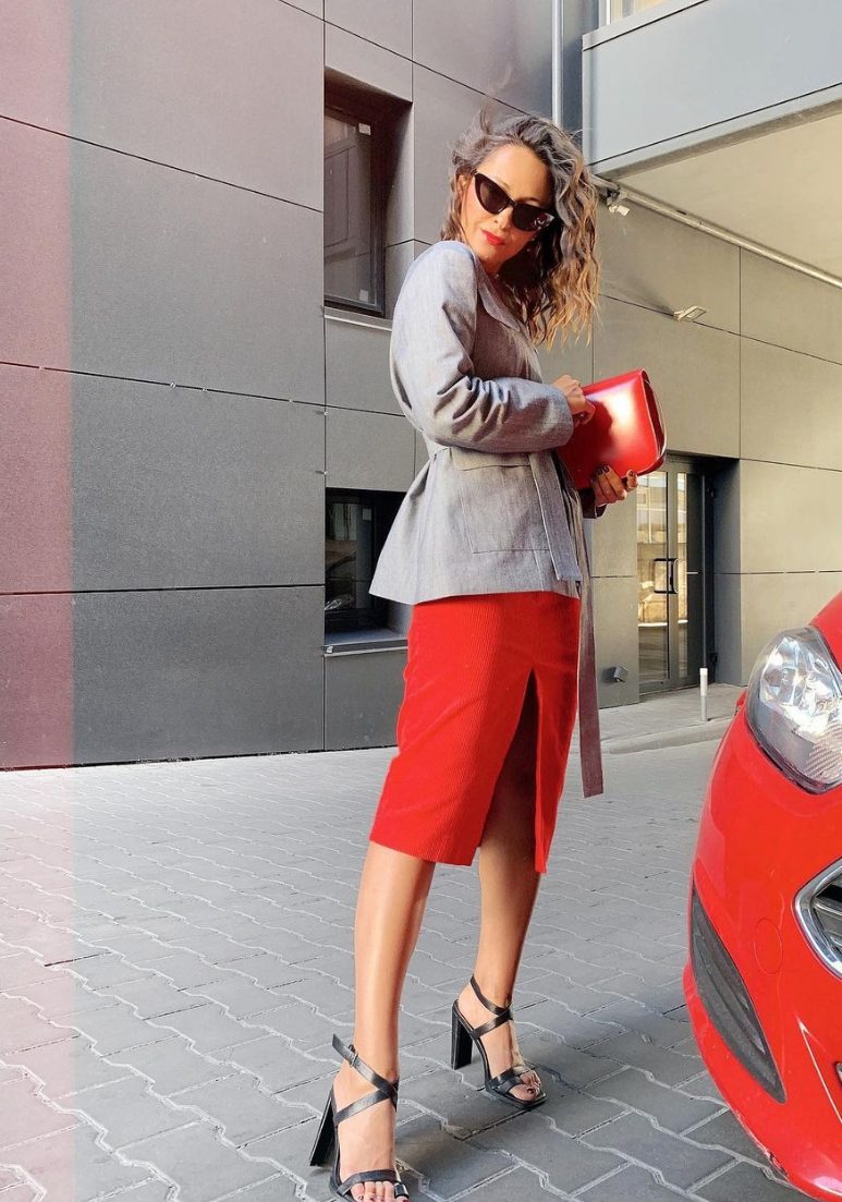 a grey jacket with a sash, a red midi skirt with a slit, a red bag and criss cross black shoes for work