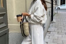 a neutral oversized sweater, white trousers, black slippers, a woven bag with black handles