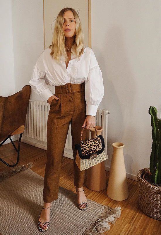 a white oversized shirt with pleated sleeves, rust-colored high waisted pants, floral print shoes and a woven bag with a leopard print