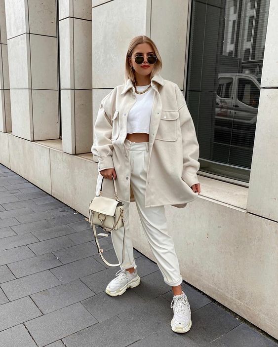 an all-neutral spring outfit with a white cropped top, creamy trousers, a creamy shirt jacket, neutral trainers and a creamy bag