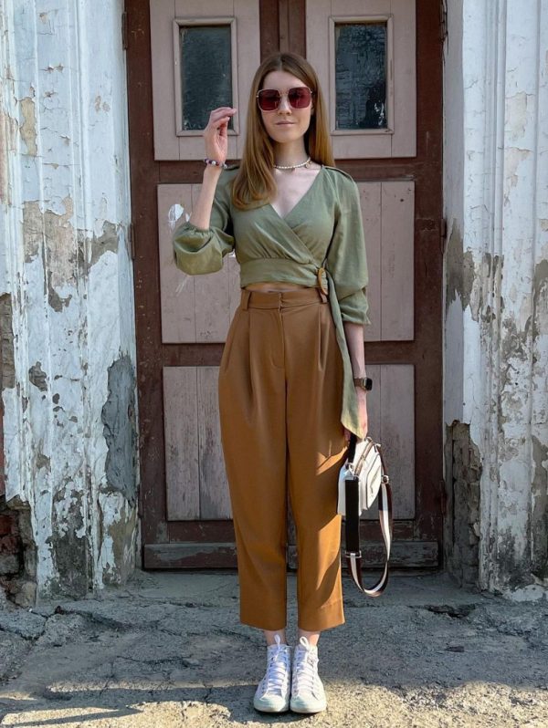 an olive green puff sleeve crop top, rust-colored high waisted trousers, white high top sneakers and a white bag