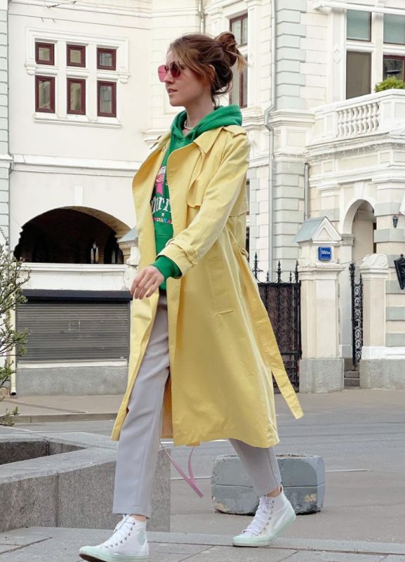grey trousers, a bright green hoodie, a yellow trench, white high top sneakers and statement sunglasses