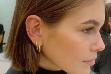 a double lobe piercing done with statement hoops and a double helix piercing done with tiny gold studs by Kaia Gerber