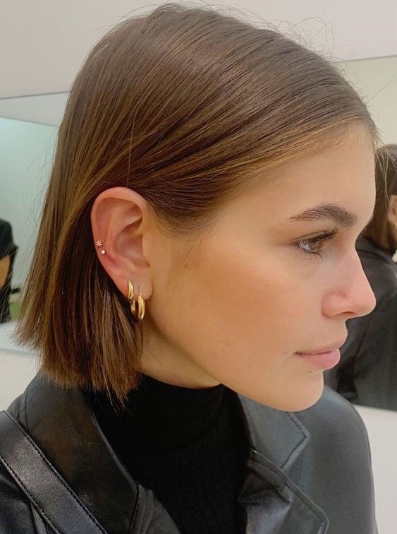 a double lobe piercing done with statement hoops and a double helix piercing done with tiny gold studs by Kaia Gerber