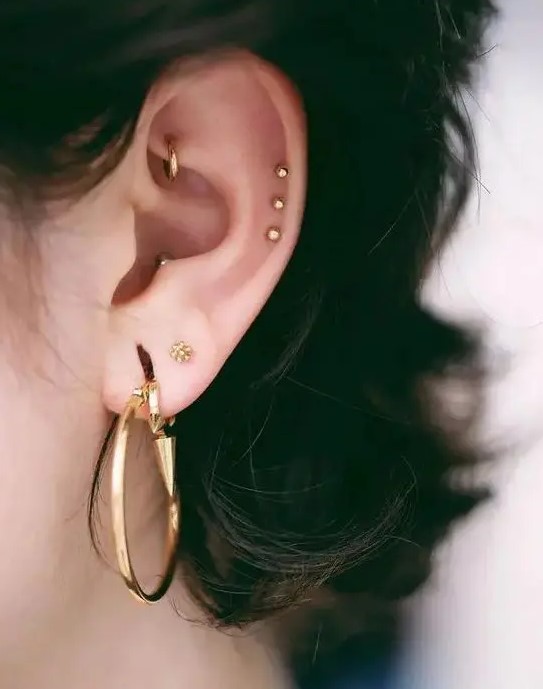a double lobe, a rook, a triple helix, a conch piercing done with statement gold hoops and beautiful gold studs for a stylisha nd edgy look