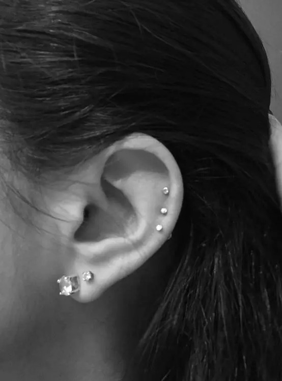 elegant ear styling with a double lobe piercing with large studs and a triple helix piercing with tiny matching studs is wow