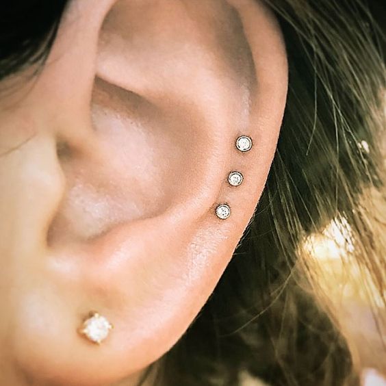 a triple helix piercing done with rhinestone studs and a beautiful gold stud in the lobe is a stylish idea for a modern and bold look
