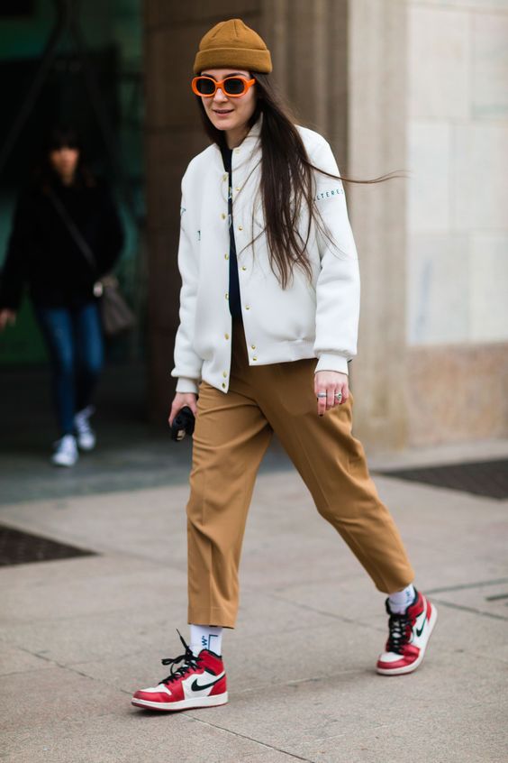 a white bombar jacket, rust-colored cropped trousers, red trainers, white socks and a mustard beanie on top