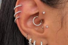 13 glam ear styling with stacked lobe and helix and flat piercings, a tragus, a forward helix and a daith piercing