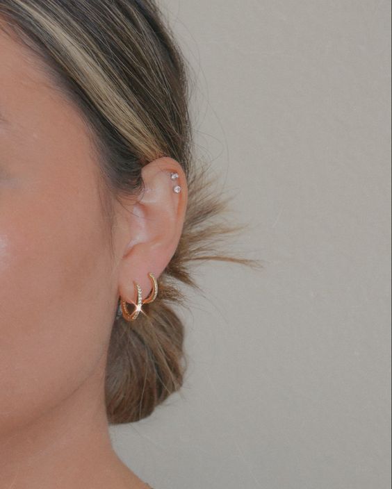 modern and glam ear styling with gold hoop earrings in the lobe and a double helix piercing done with pretty studs