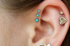 17 bold and girlish ear styling with a double lobe piercing with a turquoise and heart stud, a double helix piercing with gold studs and a triple forward helix piercing with turquoise studs
