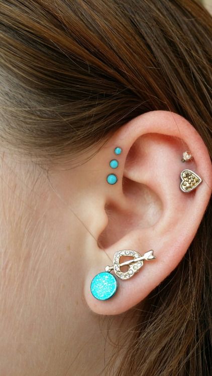 bold and girlish ear styling with a double lobe piercing with a turquoise and heart stud, a double helix piercing with gold studs and a triple forward helix piercing with turquoise studs