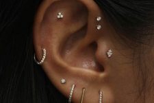 19 a beautifully curated ear with several lobe, a helix, a flat, a double forward helix and a tragus piercing all done with pretty studs and gold and rhinestone hoops