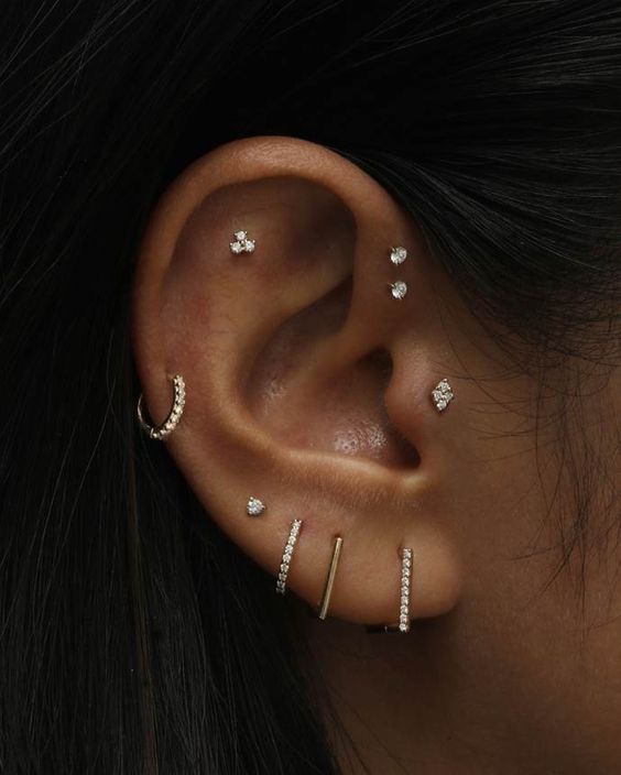 a beautifully curated ear with several lobe, a helix, a flat, a double forward helix and a tragus piercing all done with pretty studs and gold and rhinestone hoops