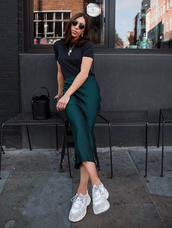 a black t-shirt, an emerald midi slip skirt, white and grey trainers and a black butcket bag for a romantic look