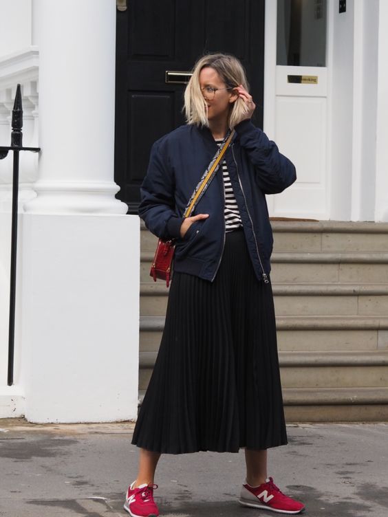 a navy and white t shirt, a black pleated midi skirt, a navy bomber jacket, red trainers and a red crossbody bag