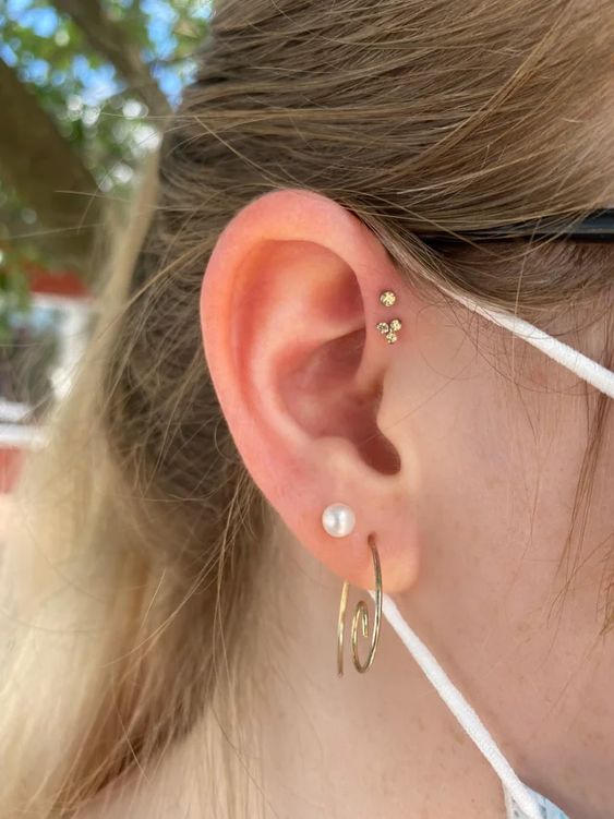 fab and chic ear styling with a double forward helix piercing done with pretty gold studs, a double lobe piercing with a pearl stud and a whimsy earring