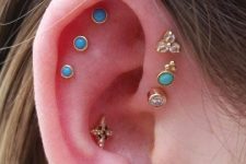 23 a bold ear with a triple flat piercing done with blue studs, a triple forward helix piercing with mismatching gold studs and a conch piercing