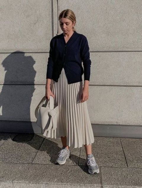 a navy cardigan, a creamy pleated midi skirt, grey trainers and a creamy bucket bag for a fashion statement