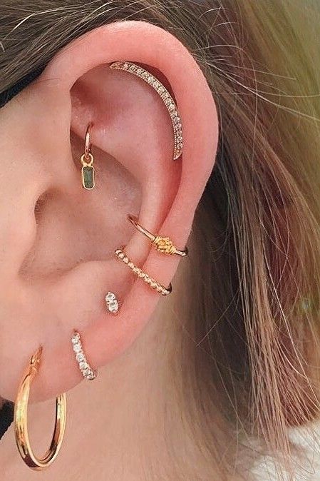 a boldly styled ear with stacked lobe, a rook, a helix and a double conch piercing with various gold hoops and studs