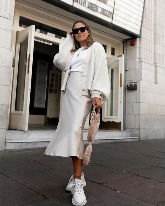 a stylish neutral work look with a white t-shirt, a slip mermaid skirt, white trainers, a white chunky cardigan with puff sleeves
