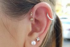 25 creative and eclectic ear styling with a double lobe piercing with a rhinestone and a pearl stud, a hoop in the helix, a double forward helix piercing with gold studs