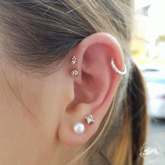 creative and eclectic ear styling with a double lobe piercing with a rhinestone and a pearl stud, a hoop in the helix, a double forward helix piercing with gold studs