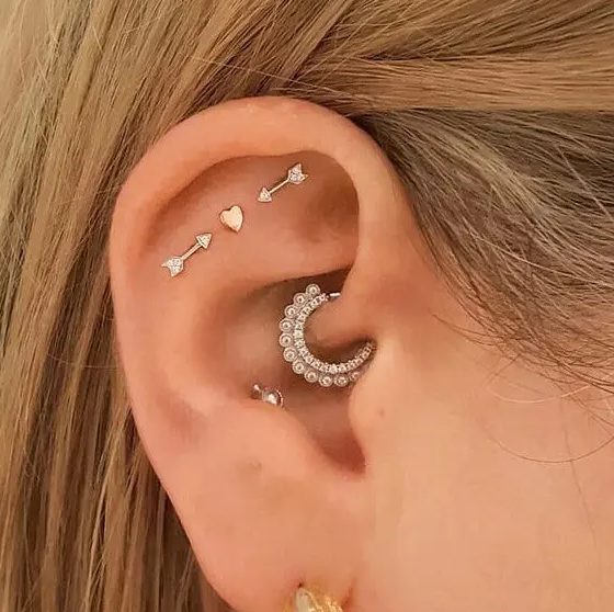 creative ear styling with a triple flat, daith, conch and lobe piercing, with heart and arrow studs and a rhinestone hoop