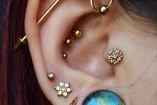 36 a boldly curated ear with stakce dlobe piercings, an industrial one, a tropical conch, a helix and a tragus piercing done with rhinestone gold studs, a bold blue one