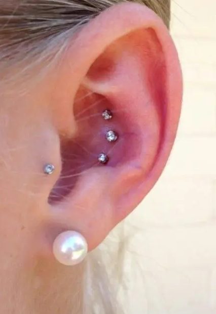 a stylish ear with a triple conch piercing, a tragus one done with rhinestone studs and a pearl in the lobe is a bold and chic idea with a touch of classics