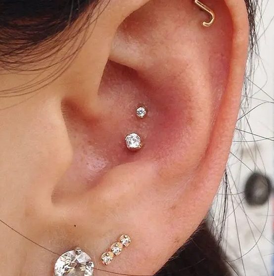 lovely ear styling with a double conch piercing with gold studs, stacked lobe peircings with studs and a flat piercing with a monogram earring