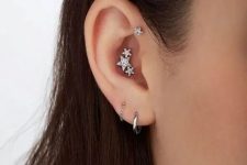 40 stacked lobe piercings with silver hoop earrings, a triple conch piercing with a whole constellation of studs and a forward helix piercing with a matching stud