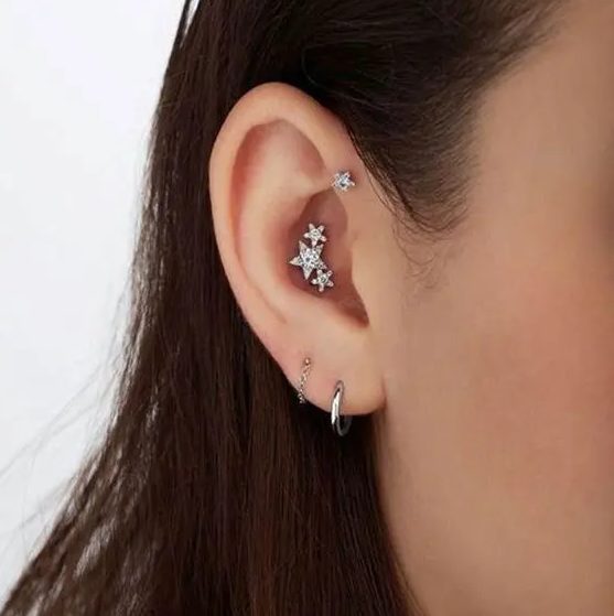 stacked lobe piercings with silver hoop earrings, a triple conch piercing with a whole constellation of studs and a forward helix piercing with a matching stud