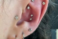 41 a chic ear with stacked lobe, a double conch, a rook, a helix and a tragus piercing done with rhinestone studs and a couple of hoops
