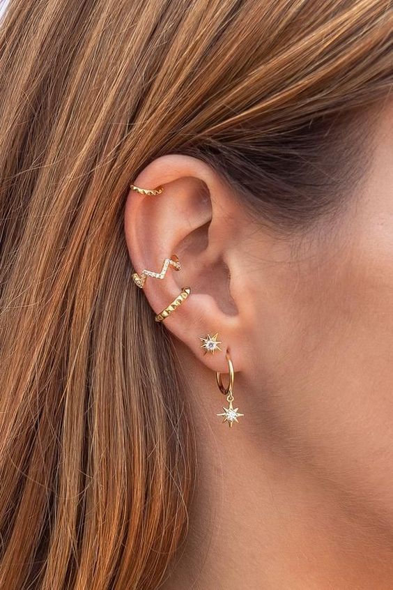 a chic ear done with stacked lobe piercings with celestial earrings, a double conch piercing with hoops and a helix piercing
