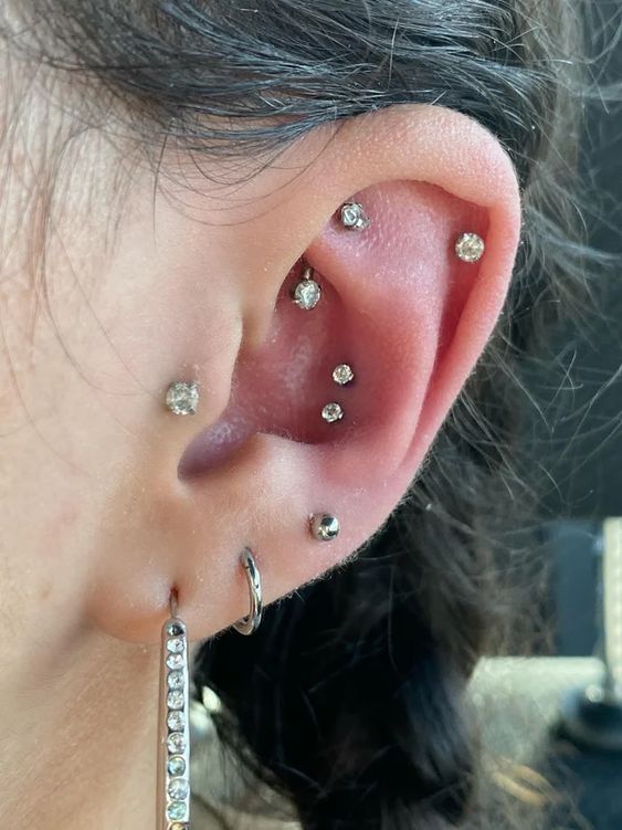 a chic ear with stacked lobe, a double conch, a rook, a helix and a tragus piercing done with rhinestone studs and a couple of hoops