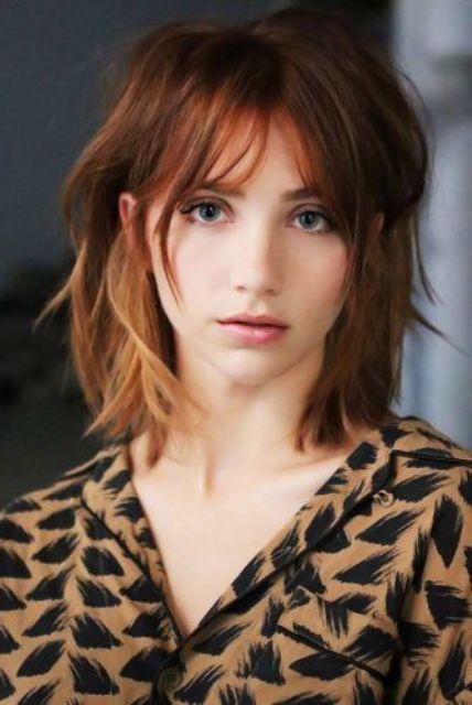 a copper shoulder length layered and messy bob with brighter highlights and usual and overgrown bangs is bold