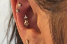 a couple of conch piercings with a white gold tri-prong gem and a yellow gold piece, stacked lobe piercings and a double flat one with pretty studs