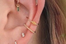 a gorgeous glam look with stacked lobe, a double conch, a flate and a rook piercing with gold studs, gold hoops with green rhinestones