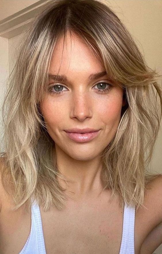 a long and messy blonde bob with a darker root and side bangs, with a lot of dimensional texture is a super chic idea