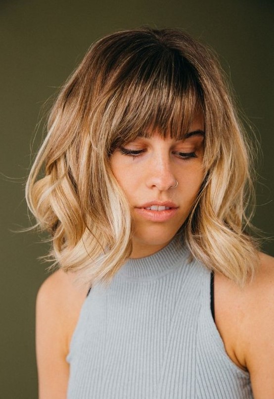 a long blonde bob with a darker root and waves plus wispy bangs for an effortlessly chic and cool look