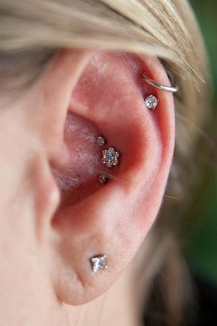 a lovely ear look with a stacked helix, a lobe and a triple conch piercing with rhinestone studs and a single hoop is a bold solution