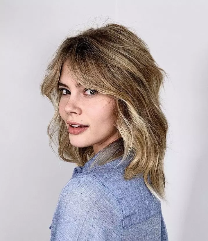 a wavy blonde long bob with layers and curtain bangs to give a 70s vibe to the look