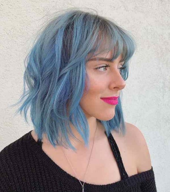 an edgy shaggy long bob with bangs done in light blue with waves that bring texture and movement to the look