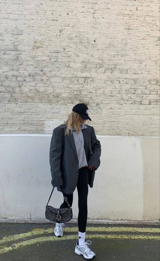 a grey zip jumper, black leggings, a black oversized blazer and a cap, grey trainers and white socks and a black bag