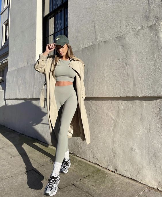 a sexy sport chic outfit with a grey crop top and leggings, grey trainers and white socks, a tan trench and a grey cap