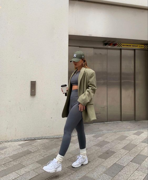 a spring athleisure look with a grey crop top and leggings, white trainers and socks, a green oversized blazer and a cap