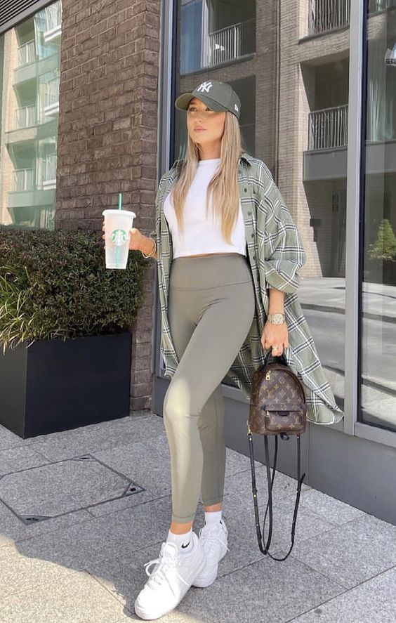 a white crop top, grey sporty leggings, white trainers and socks, a grey overshirt, a grey baseball cap and a brown backpack
