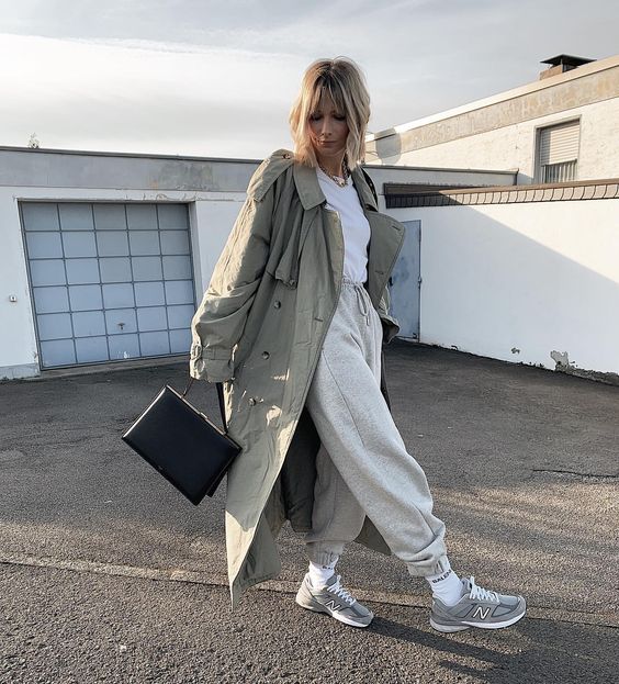 a relaxed spring outfit with a white t-shirt, grey joggers, grey trainers, white socks and a gret trench plus a black bag